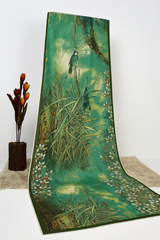 A green and gold-colored silk dupatta with a bird print, hanging beautifully over a wooden stand.