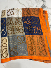 A woman standing outdoors holding a silk dupatta with a geometric moneyplant print in orange, black, and green colors.