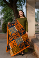 A woman standing outdoors holding a silk dupatta with a geometric moneyplant print in orange, black, and green colors.